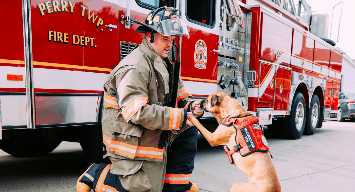 Firefighter holds dogs paws in front of fire truck