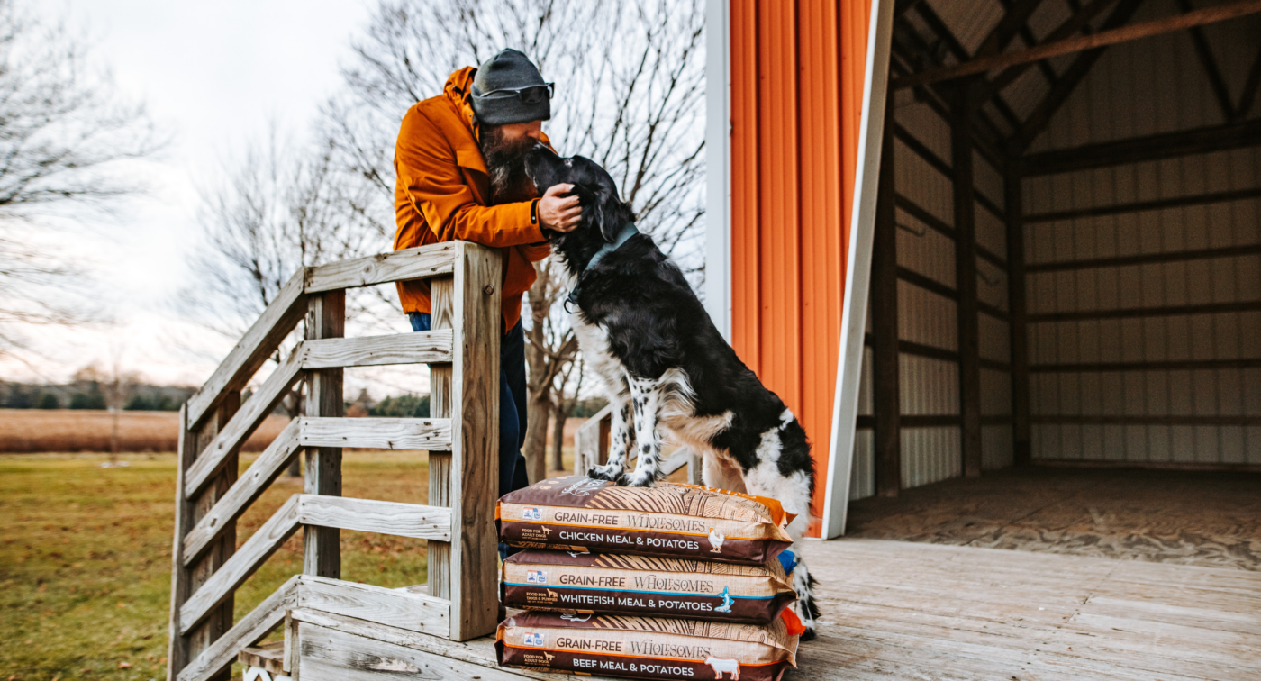 dog standing on top of Wholesomes pet food being pet by owner